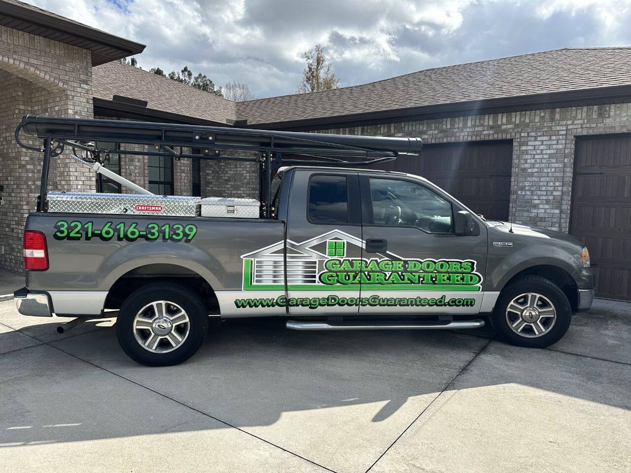 gray pickup truck with a logo for "Garage Doors Guaranteed" parked in a driveway.