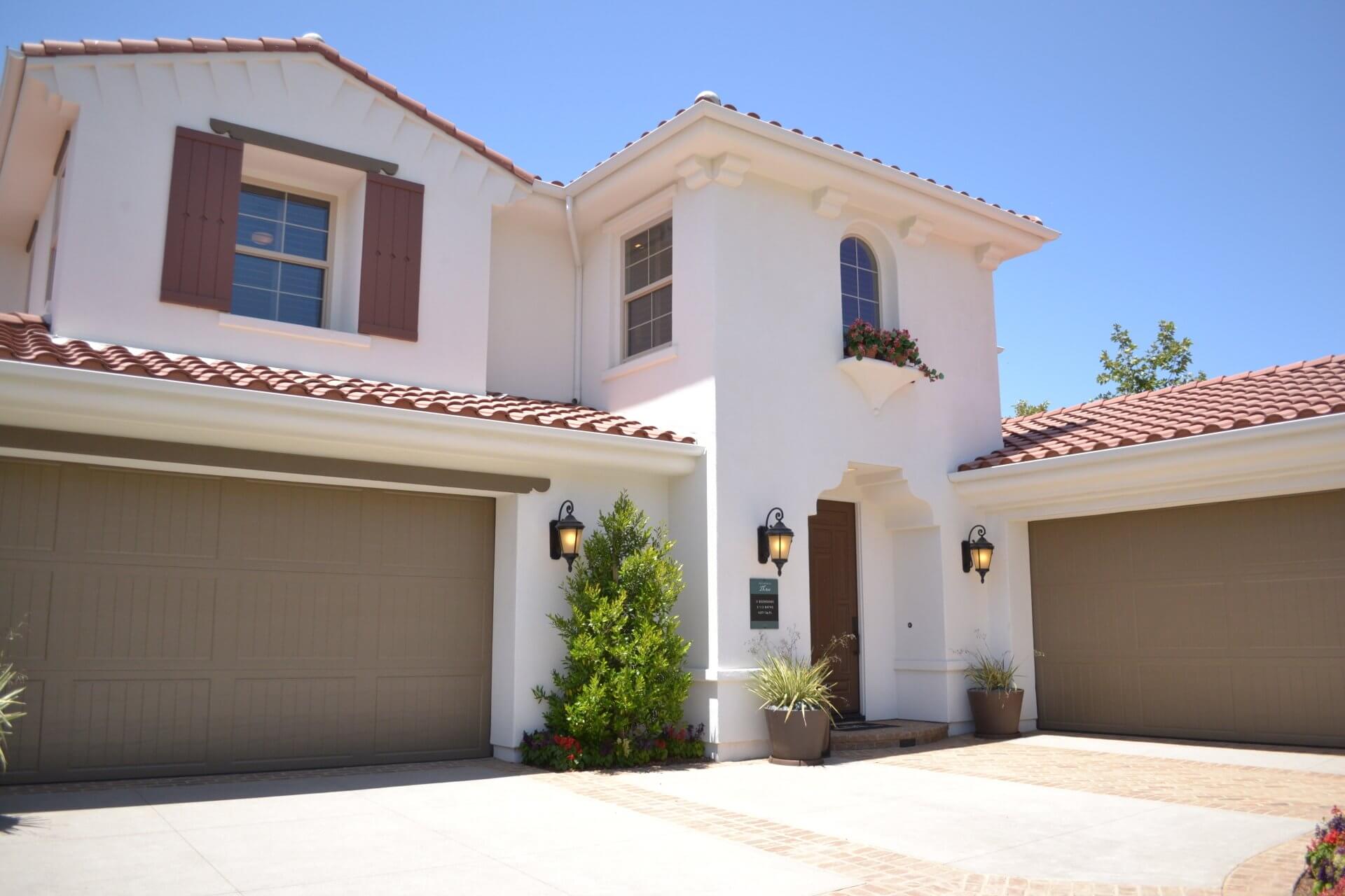 The front exterior of a large house with a tile roof and two garage doors.