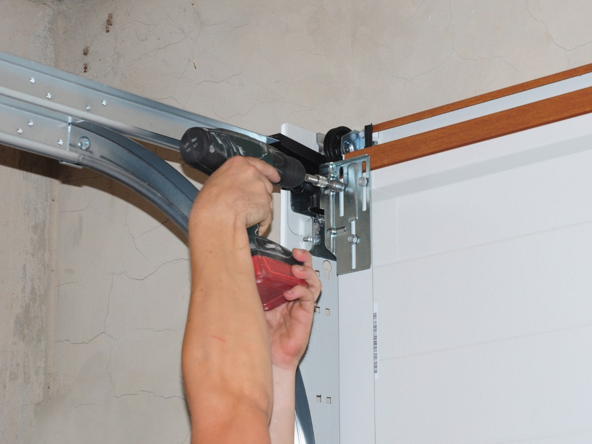 A person using a drill to install garage door tracks.