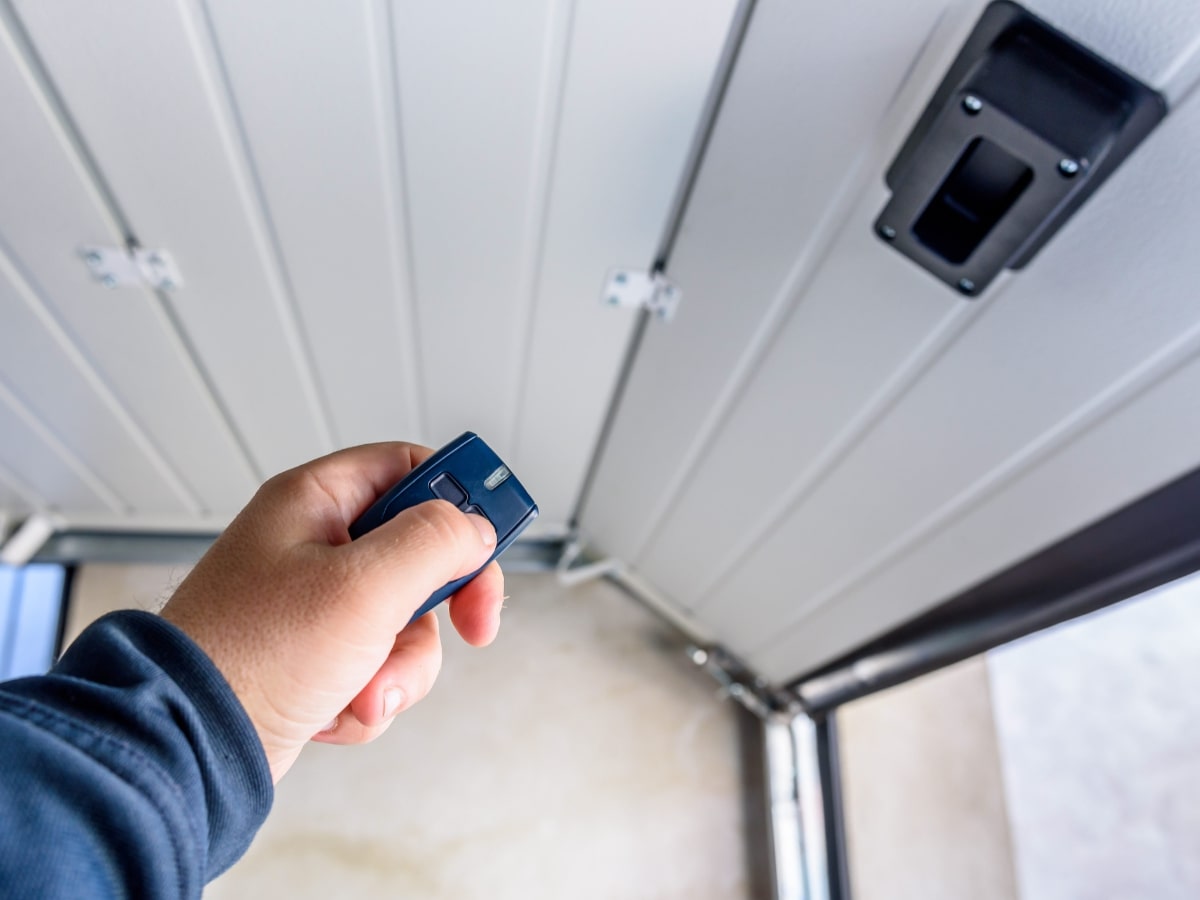 A person's hand holding a remote control to open a garage door.