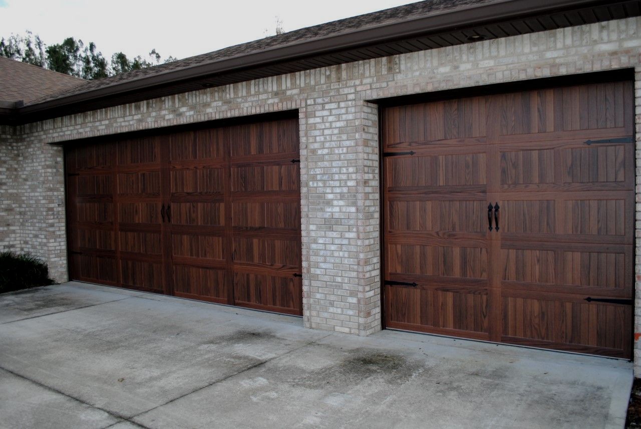 Two wood-look garage doors on a brick house.